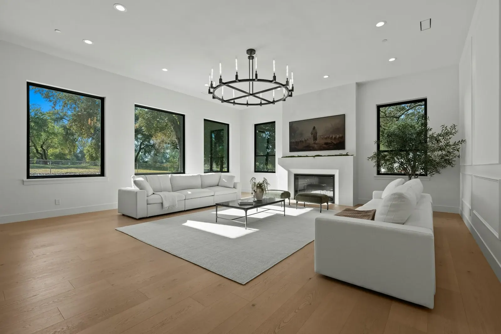 Modern living room with white sofas, fireplace, large windows, and wood flooring